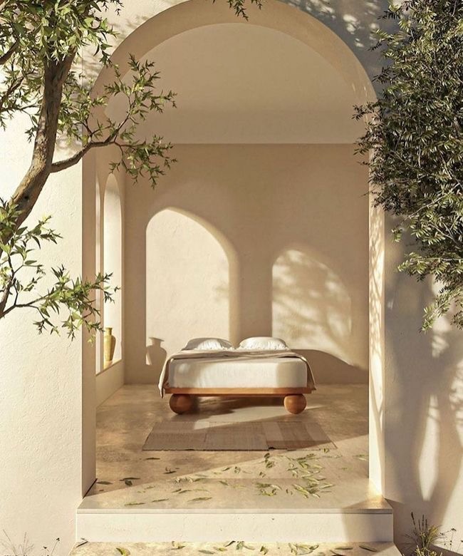 A tranquil arched space featuring a minimalist bed, soft beige tones, dappled sunlight, and surrounding olive trees for a serene vibe.